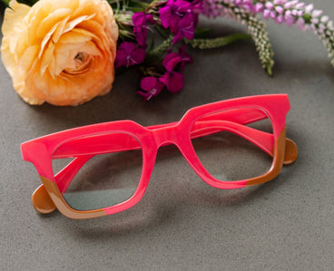 Pink glasses with brown arms on a gray surface with flowers in the background