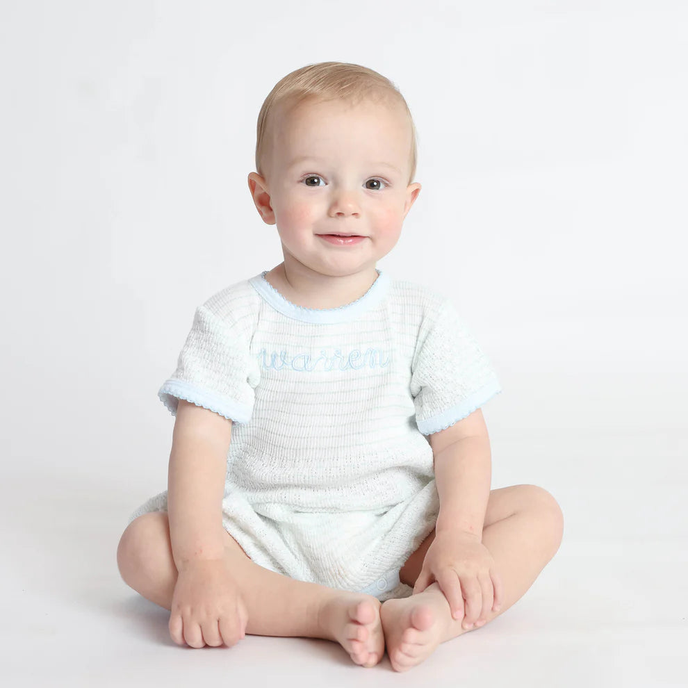 Baby wearing a blue textured romper with blue trim on a light gray background