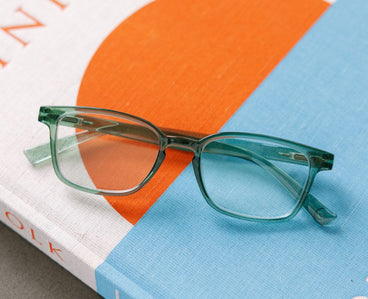 Green eyeglasses on a book with an orange and blue background