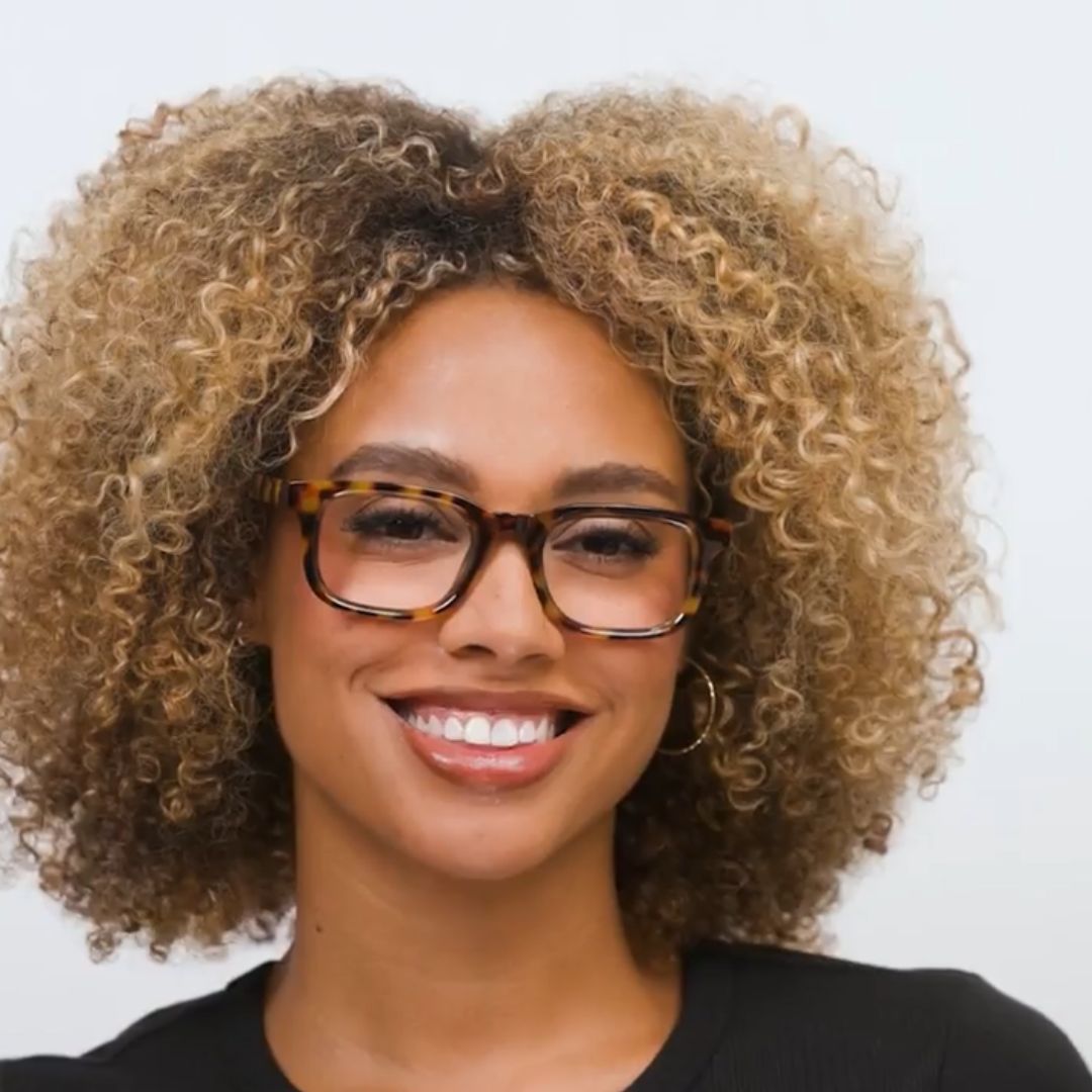 Woman with curly hair wearing glasses against a white background