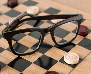 Black-framed glasses on a checkered surface with game pieces