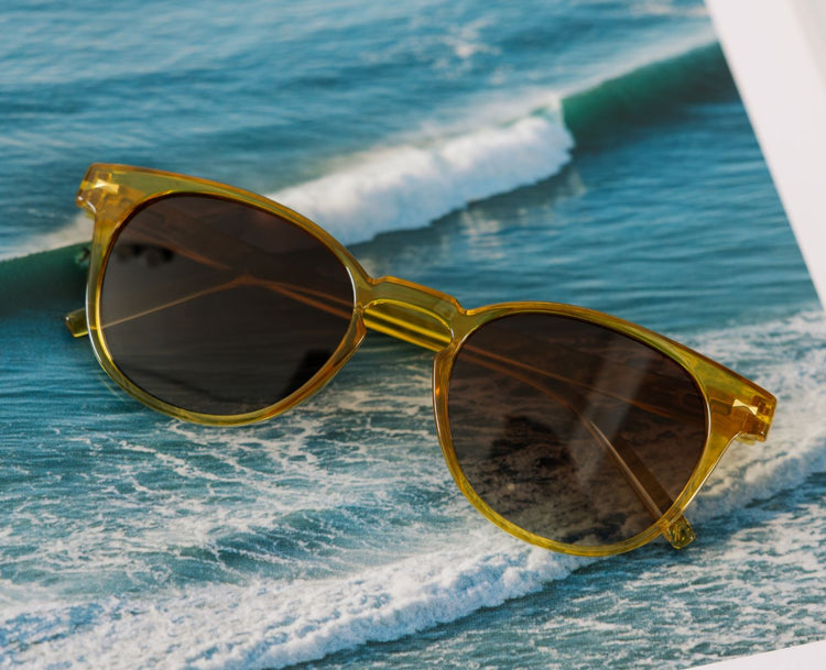 Gold-framed sunglasses on a picture of ocean waves in the background
