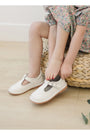 Children's feet wearing white shoes with decorative bows on a light wooden floor.