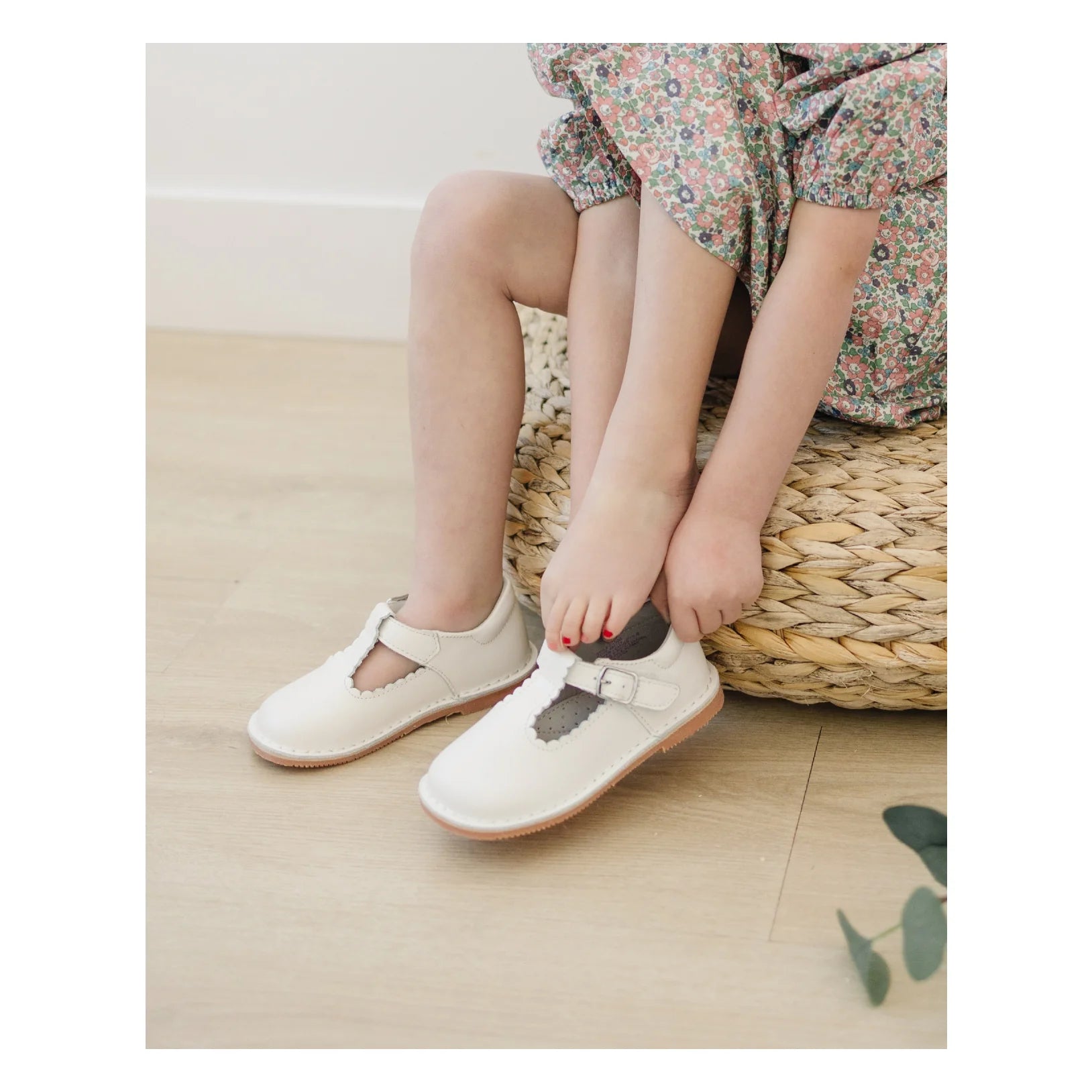 Children's feet wearing white shoes with decorative bows on a light wooden floor.
