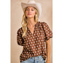 Woman wearing a brown polka dot blouse, white cowboy hat, and denim shorts against a beige background