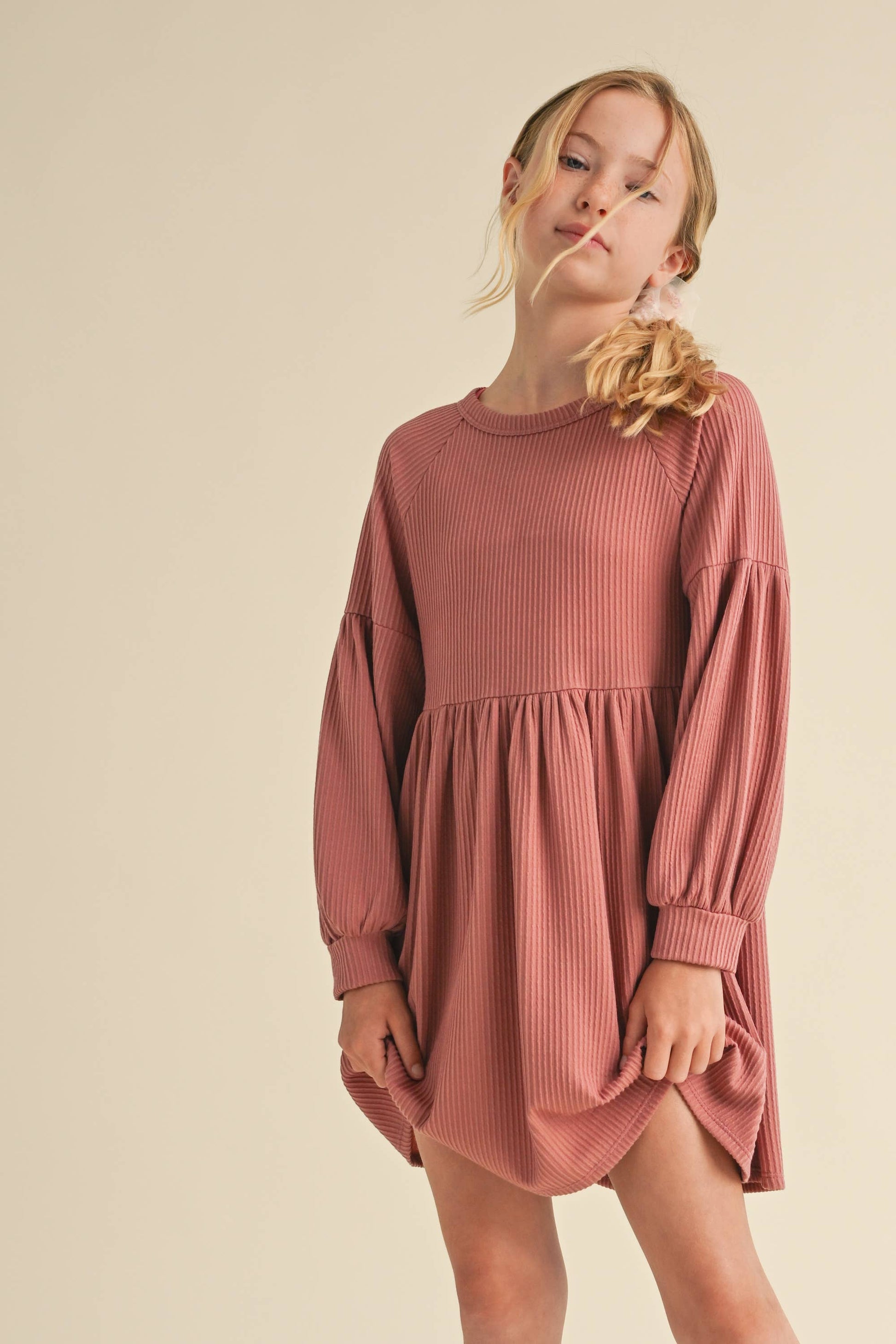 Young girl wearing a ribbed pink dress against a beige background