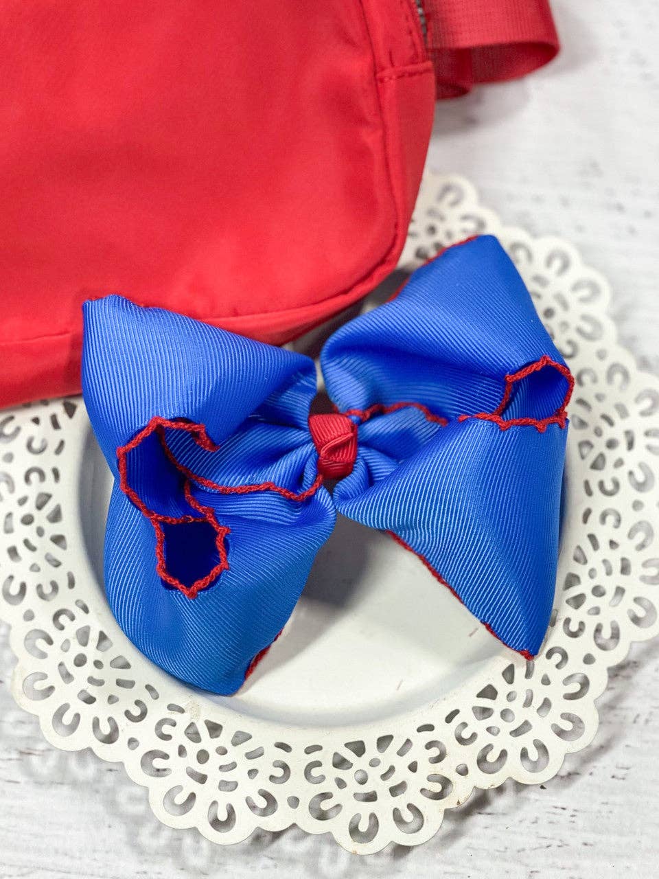 Blue hair bow with red accents on a white lace doily