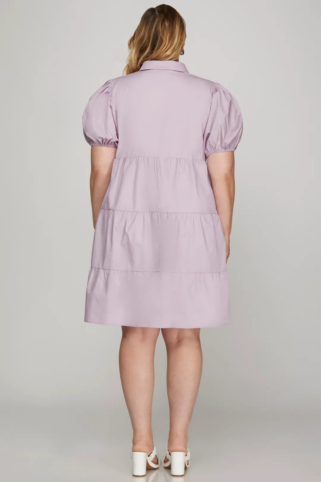 Woman wearing a light purple dress with puff sleeves on a plain background