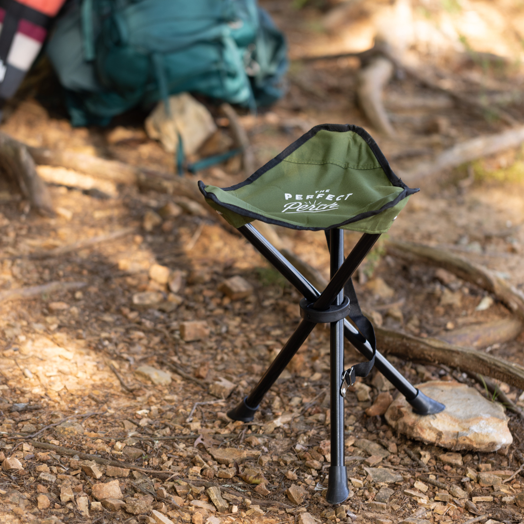Green camping stool with 'The Perfect Picnic' branding on a forest floor.