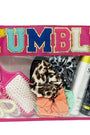 Pink zippered candy bag with clear front and bold 'TUMBLE' patch, filled with hair accessories