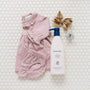 Pink baby outfit with bloomers, bottle of lotion, and hair bow on a tiled background