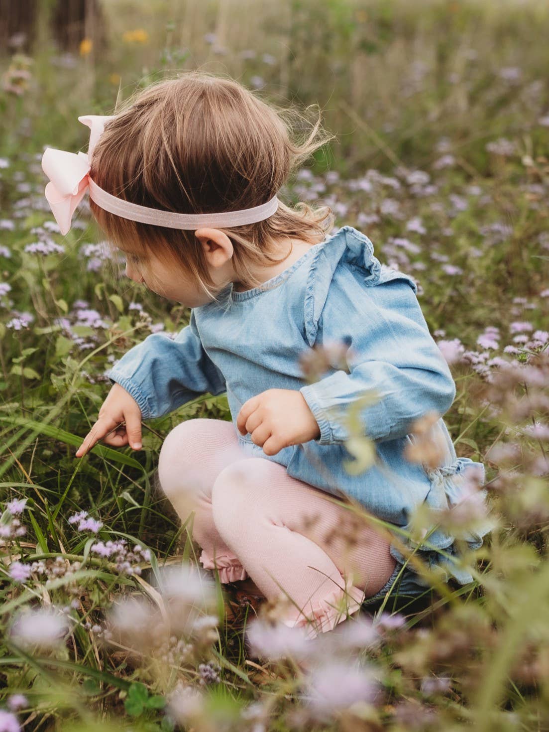 Child in a blue dress sitting in a field of flowers