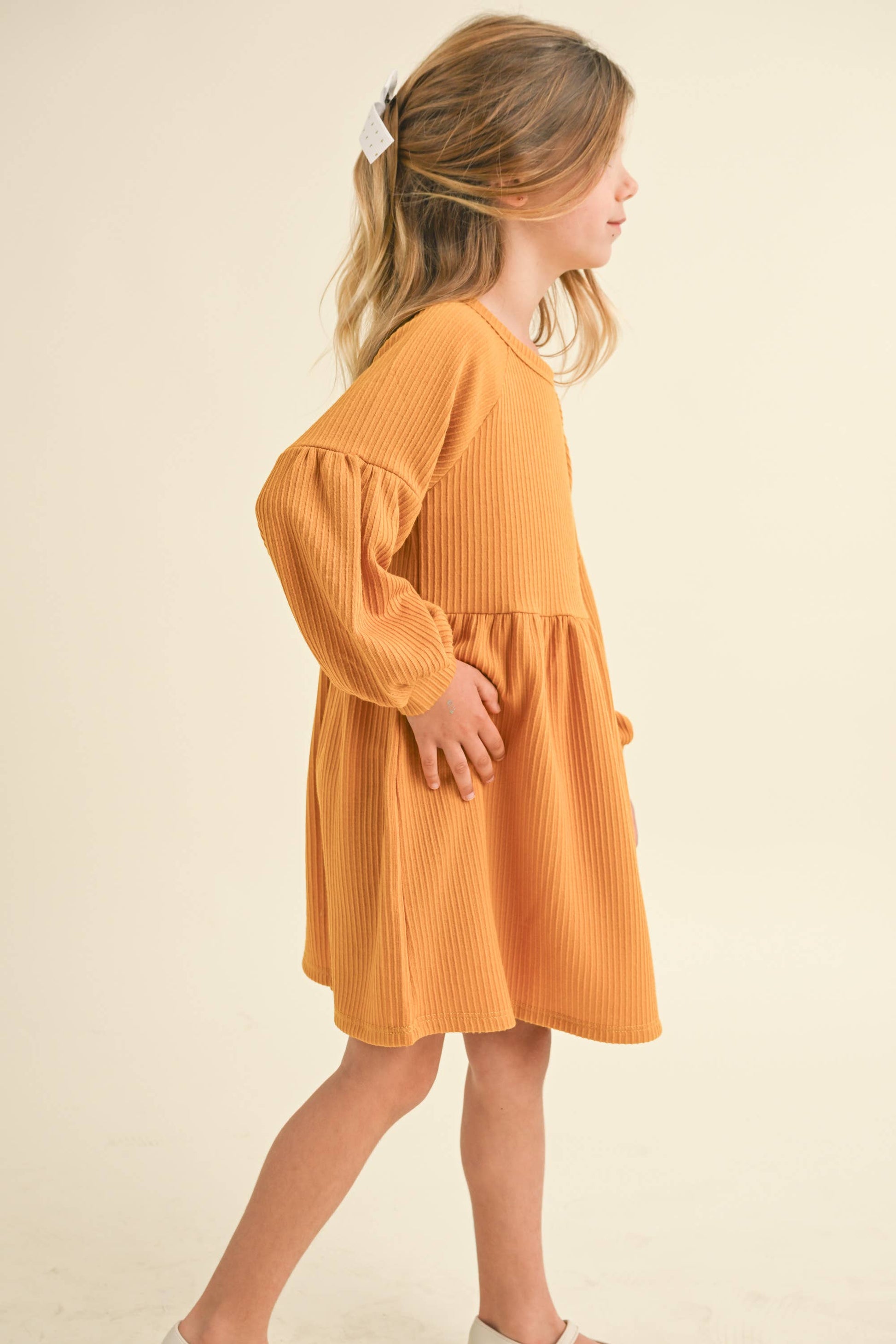 Young girl wearing a mustard yellow dress against a beige background