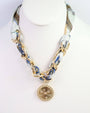 Gold chain necklace with a pendant on a mannequin head wearing a patterned scarf.
