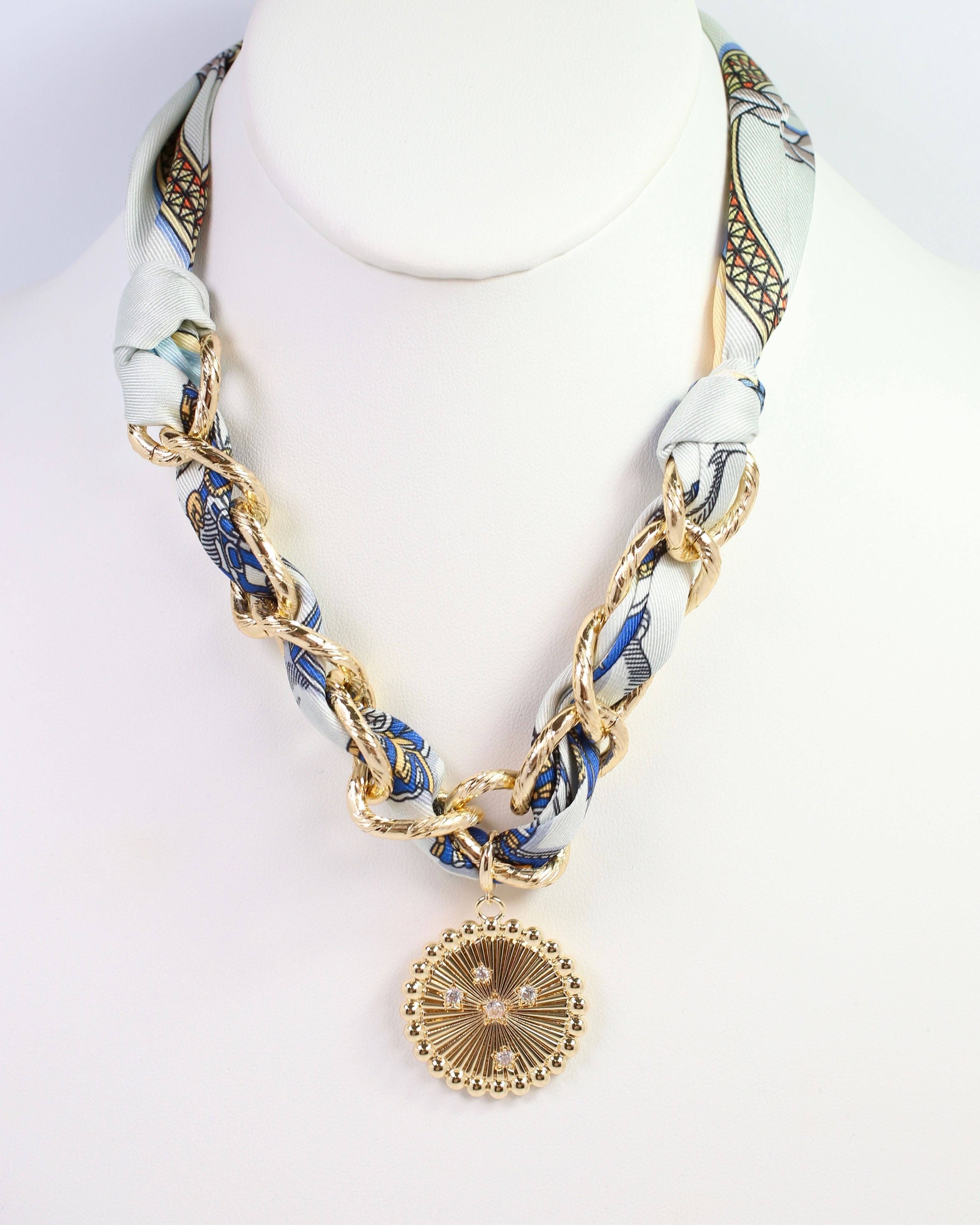 Gold chain necklace with a pendant on a mannequin head wearing a patterned scarf.