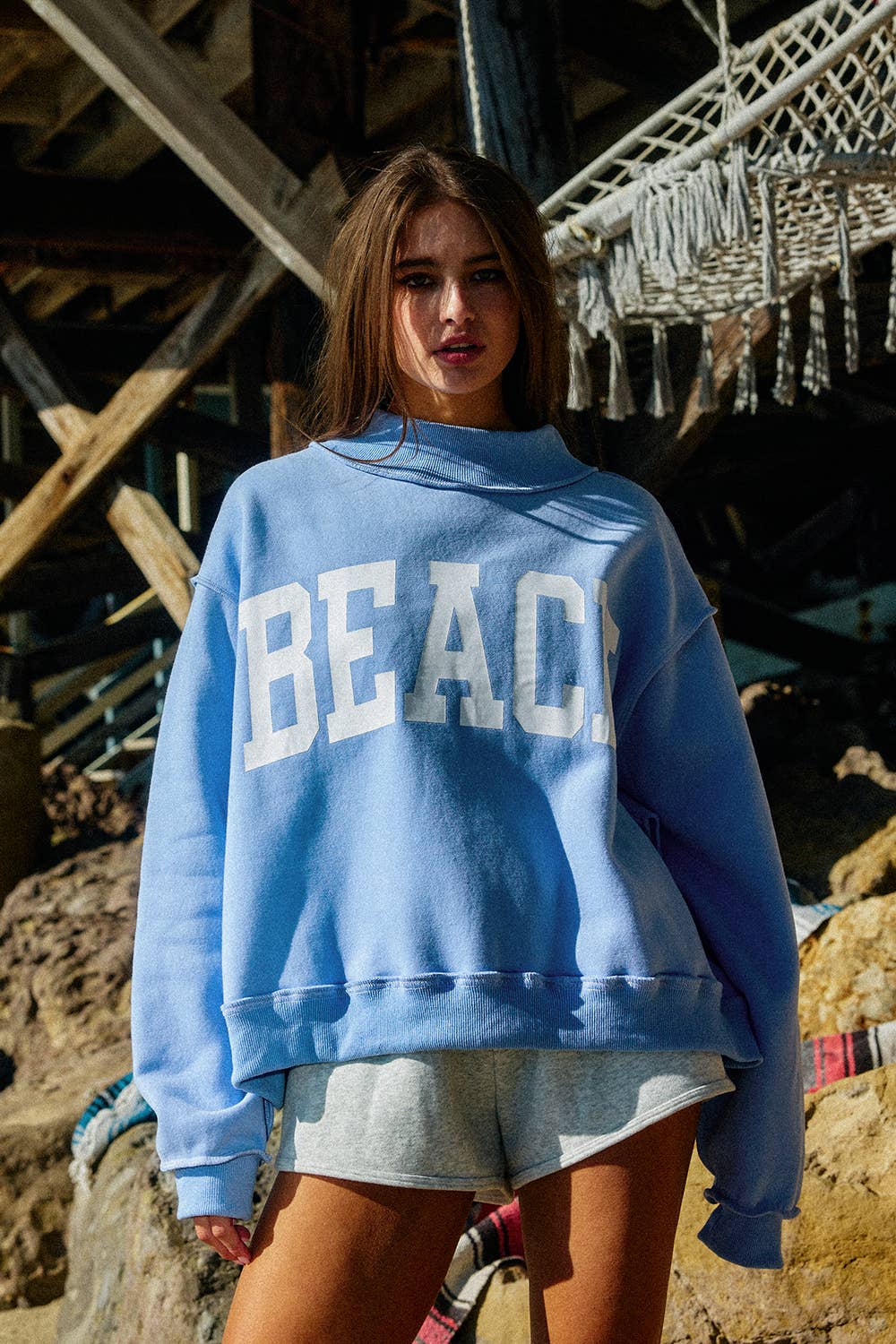 Woman wearing a blue sweatshirt with 'BEACH' text, standing on a beach.