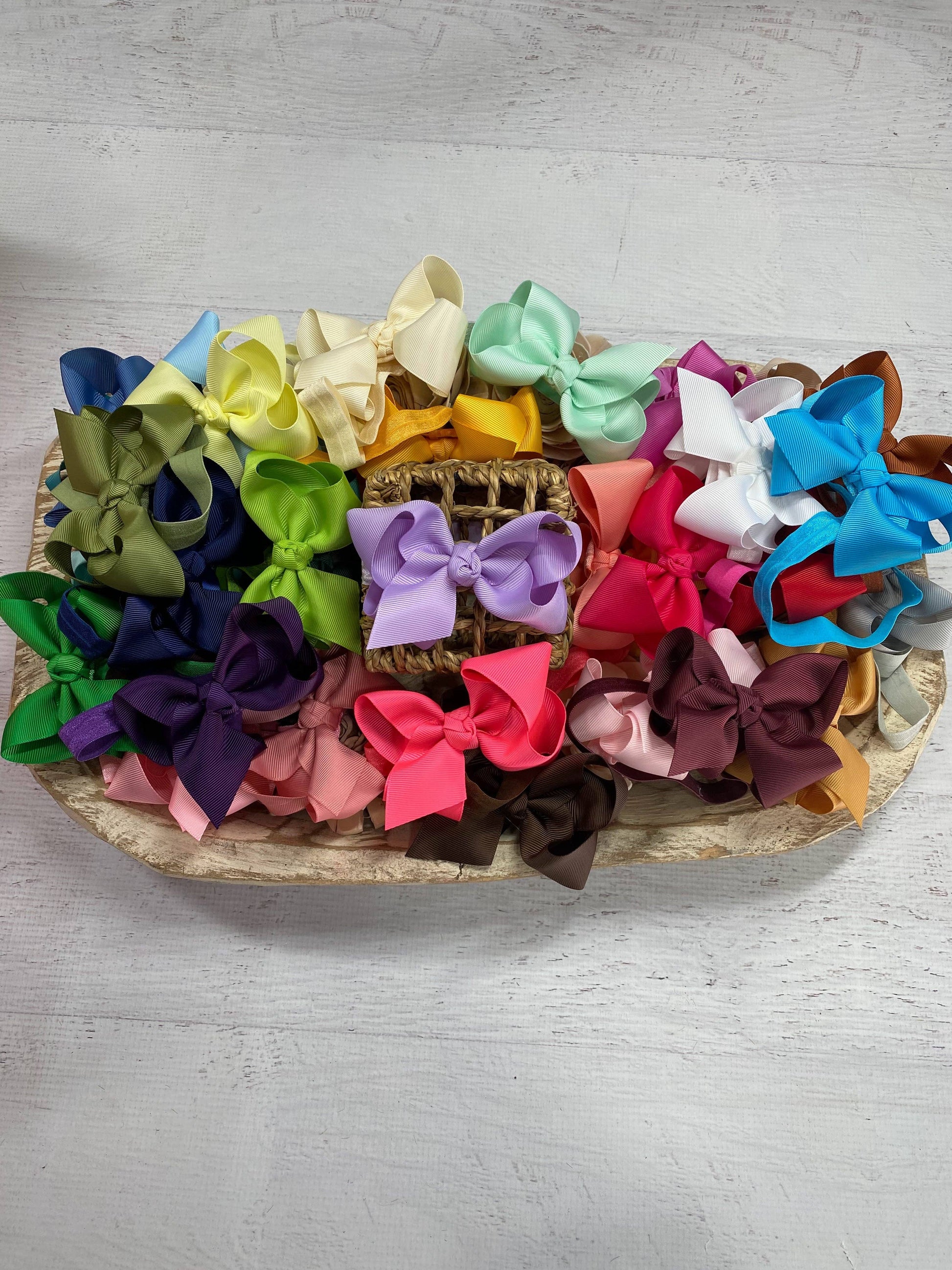 Assorted colorful hair bows on a wooden tray with a light gray background