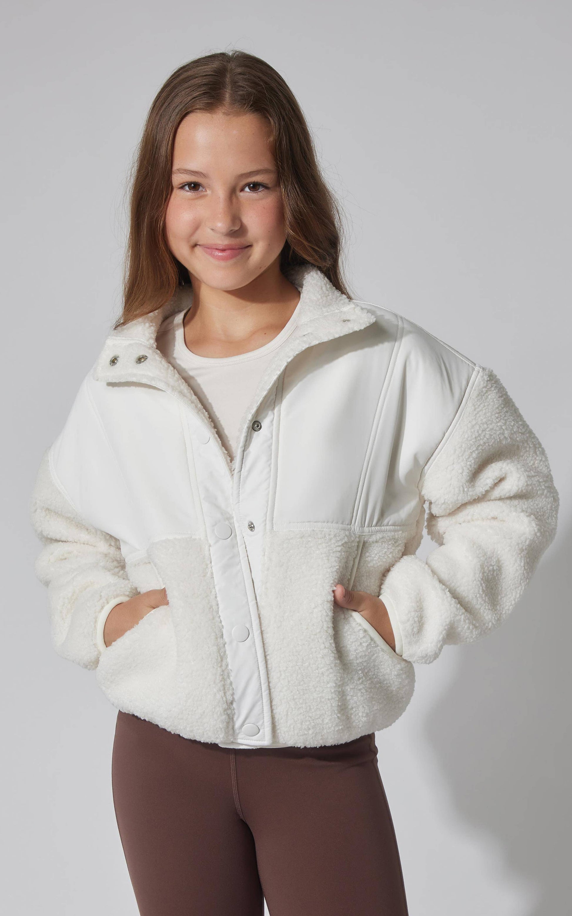 Young girl wearing a white fleece jacket against a plain background