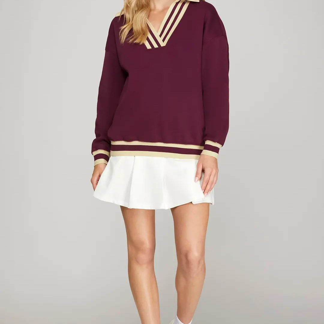 Woman wearing a burgundy sweater with gold trim and a white skirt on a gray background