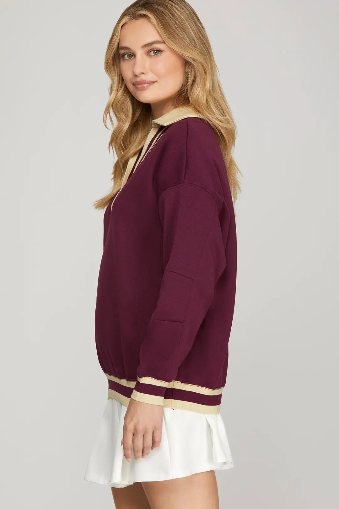 Woman wearing a maroon sweater with gold trim on a plain background