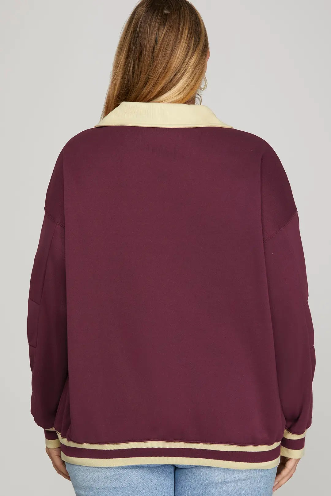 Woman wearing a burgundy sweater with cream accents on a plain background