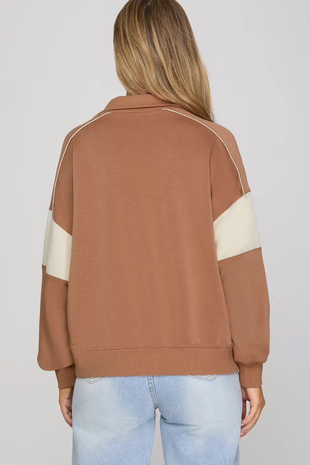 Brown sweatshirt with white stripes on sleeves worn by a person against a plain background