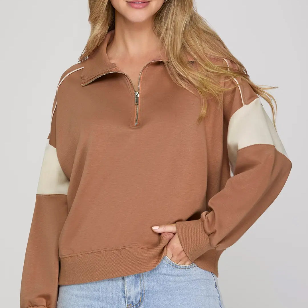 Woman wearing a brown and beige color-blocked sweater with light blue jeans on a plain background