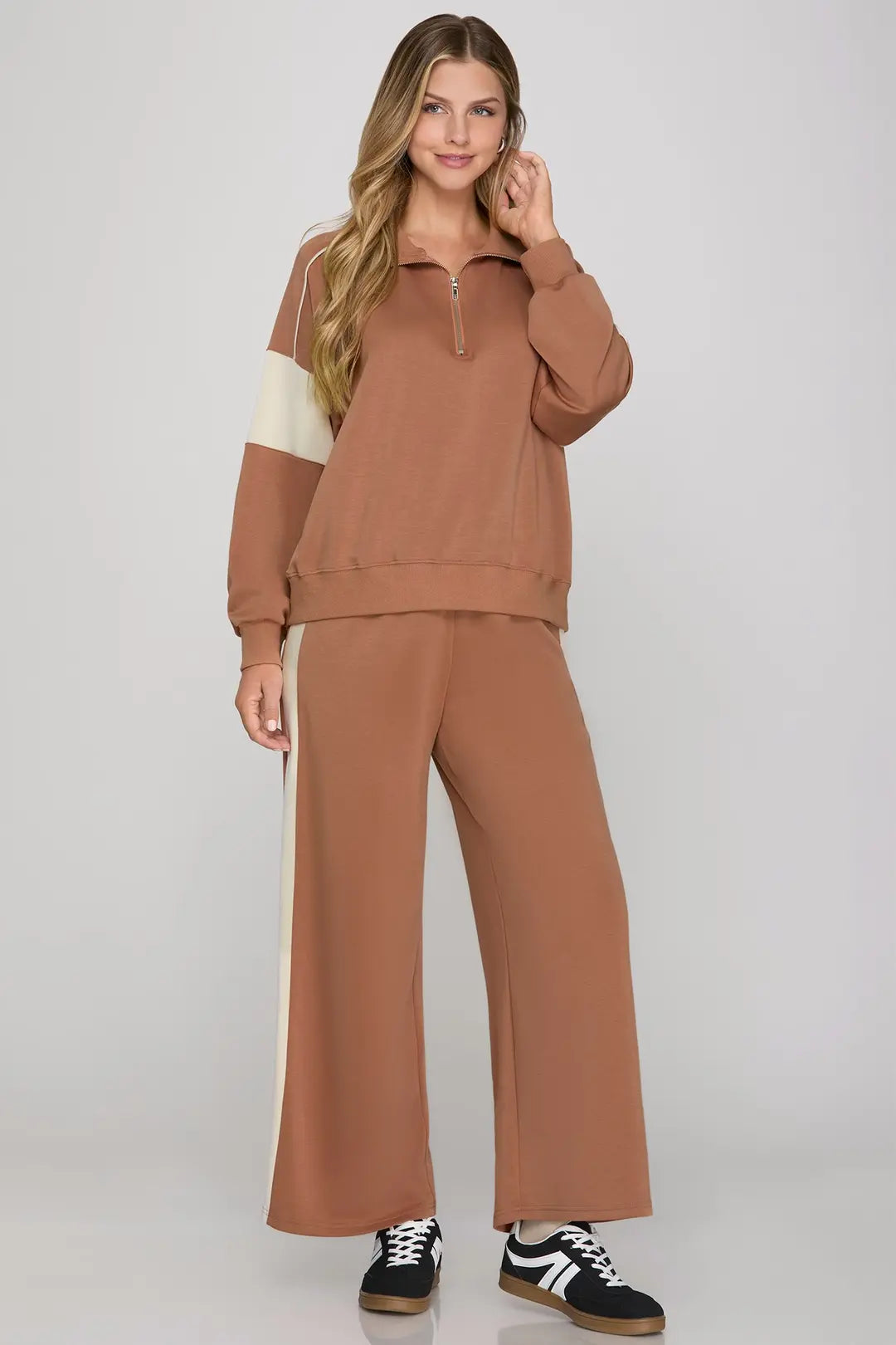 Woman wearing a brown tracksuit with white accents on a plain background