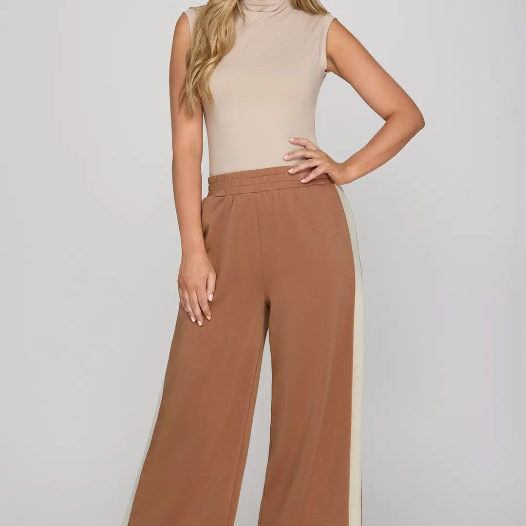 Woman wearing a beige sleeveless top and brown wide-leg pants on a white background