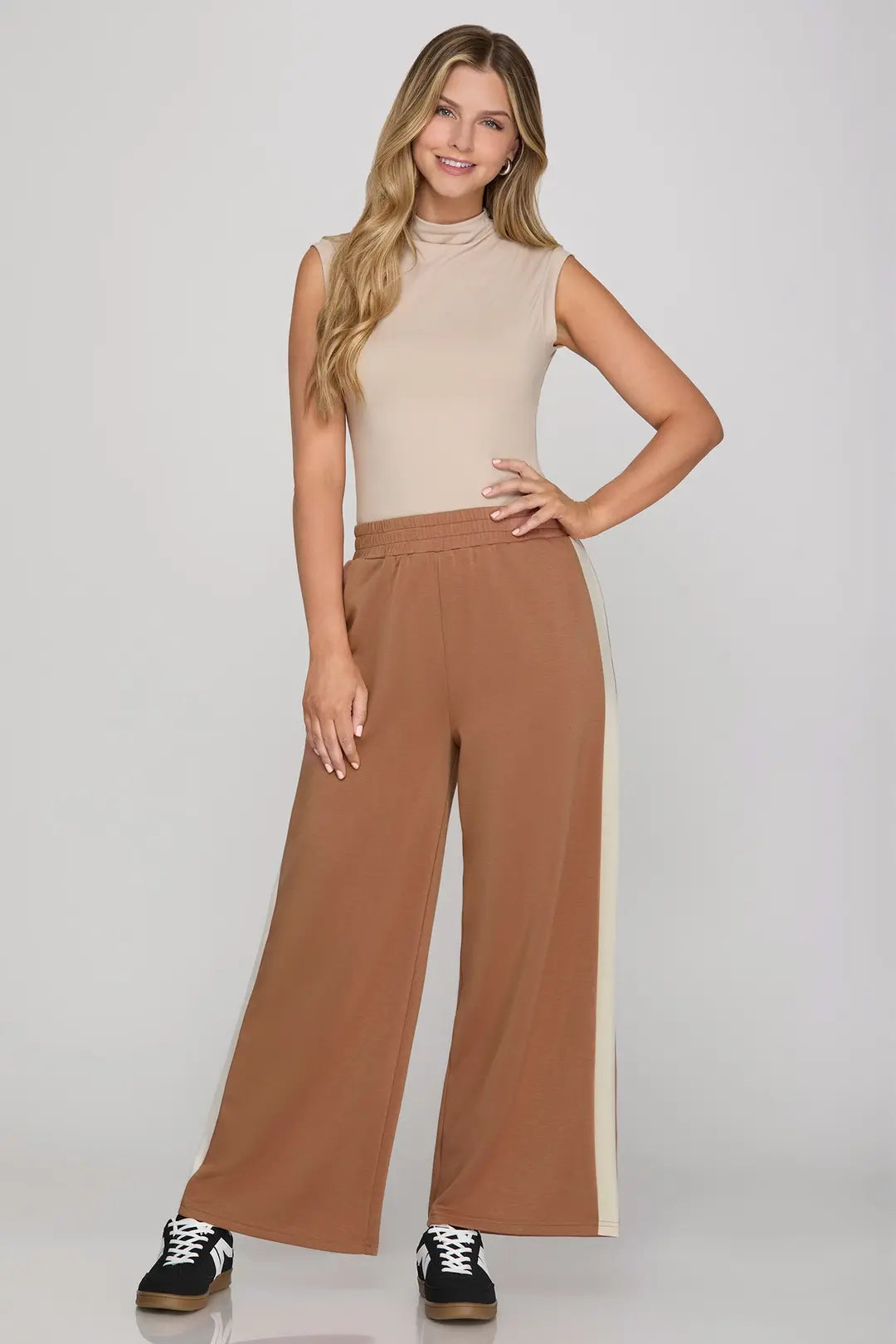 Woman wearing a beige sleeveless top and brown wide-leg pants on a white background