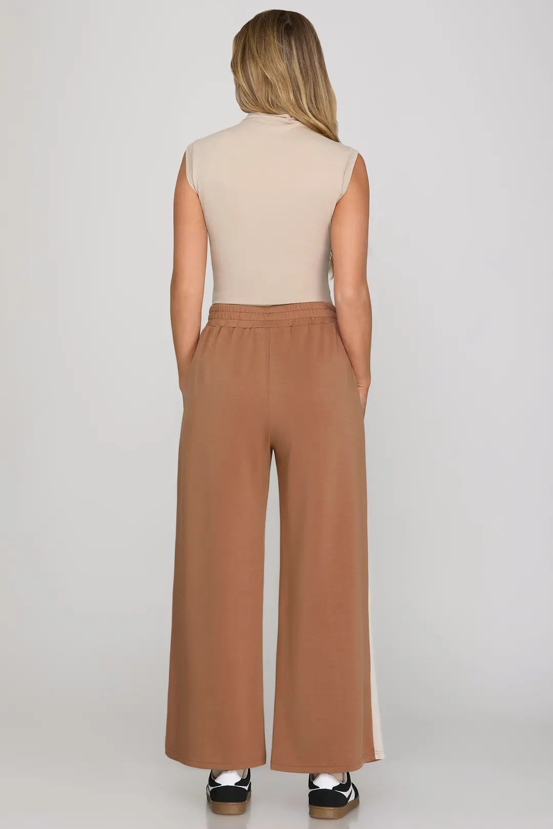 Woman wearing a beige sleeveless top and brown wide-leg pants on a white background