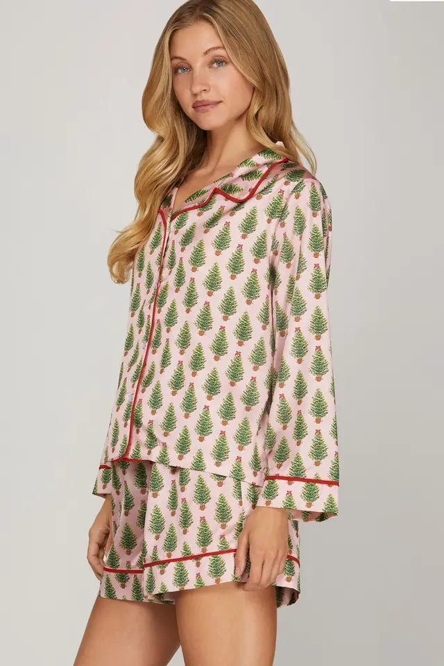Woman wearing a festive pajama set with Christmas tree pattern on a plain background