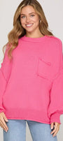 Woman wearing a bright pink sweater with a pocket on a plain background