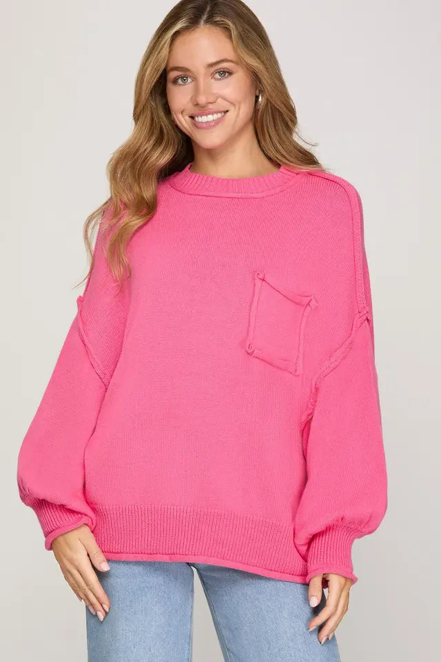Woman wearing a bright pink sweater with a pocket on a plain background