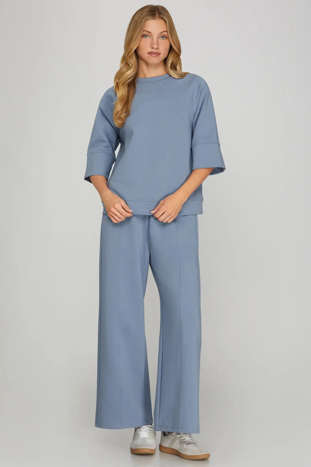 Woman wearing a blue outfit with wide-leg pants on a plain background