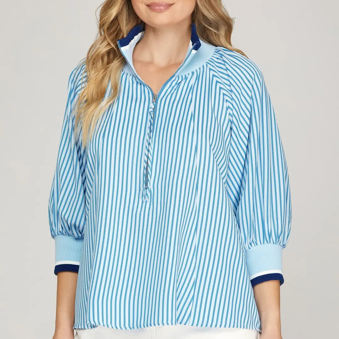 Woman wearing a blue striped shirt with white shorts on a plain background