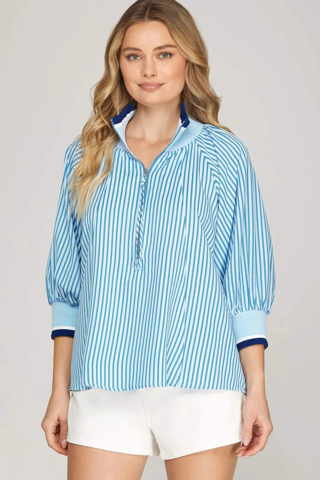 Woman wearing a blue striped shirt with white shorts on a plain background