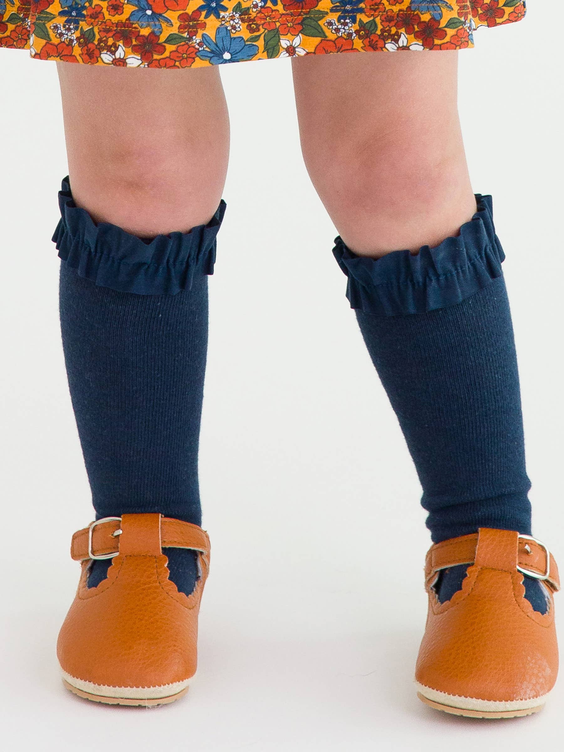 Navy knee-high socks with ruffles worn by a child, paired with orange shoes on a white background.