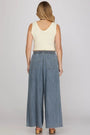 Woman wearing a cream sleeveless top and blue denim wide-leg pants on a plain background
