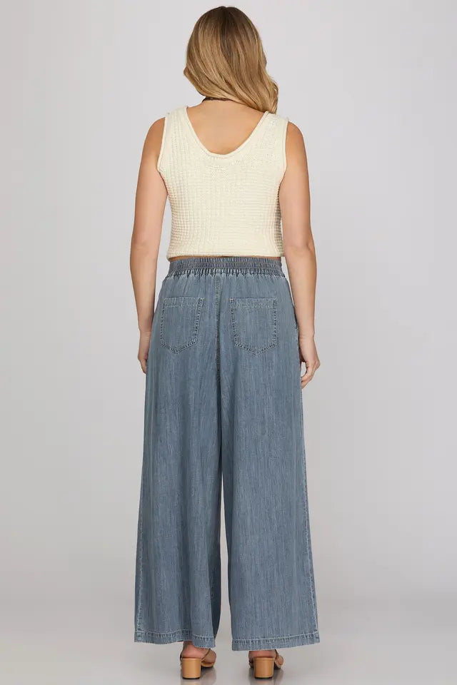 Woman wearing a cream sleeveless top and blue denim wide-leg pants on a plain background
