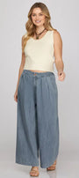 Woman wearing a cream sleeveless top and wide-leg denim pants on a plain background