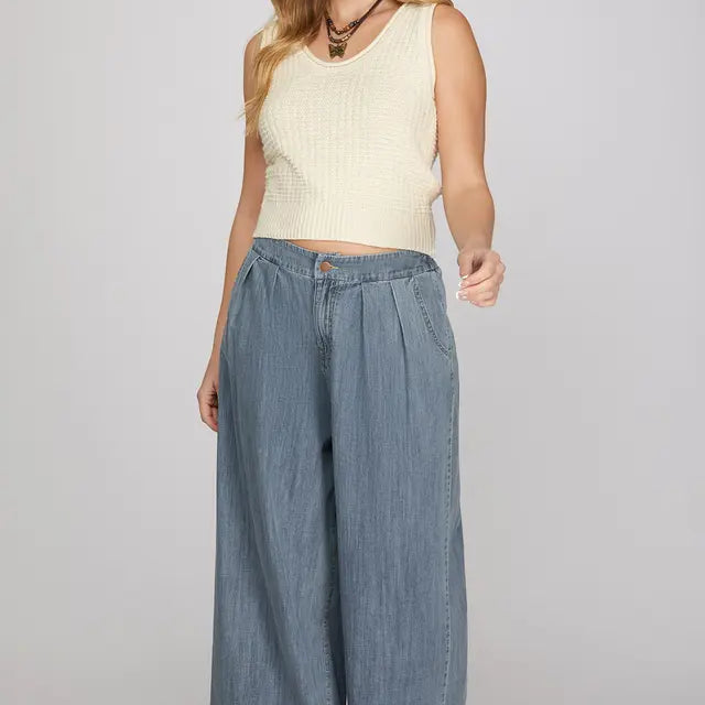 Woman wearing a cream sleeveless top and wide-leg denim pants on a plain background