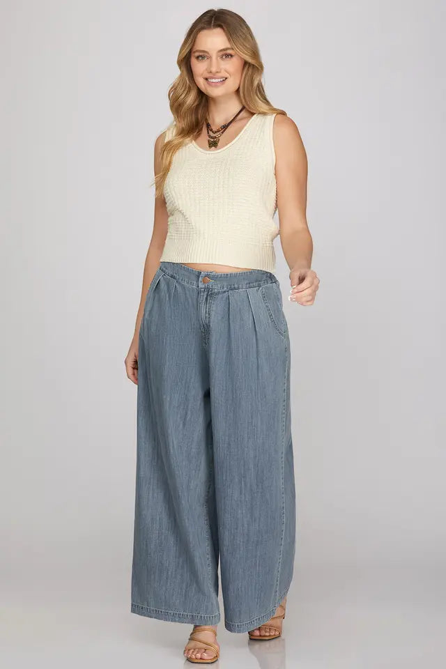 Woman wearing a cream sleeveless top and wide-leg denim pants on a plain background