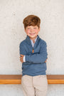 Young boy wearing a blue jacket with a white wall background