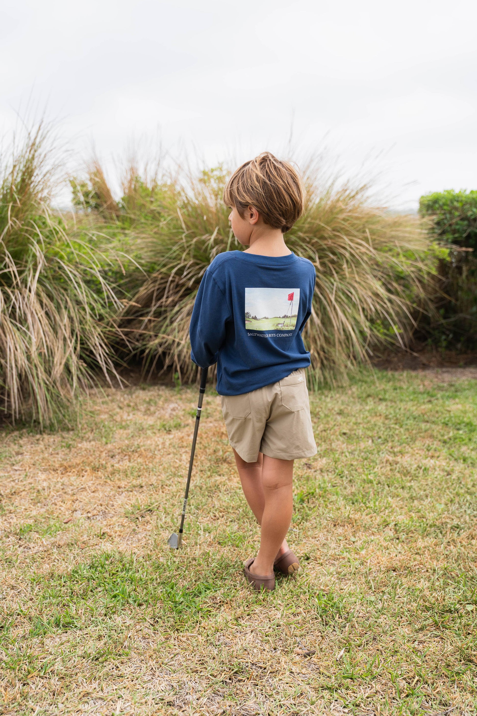 Child holding a golf club in a grassy outdoor setting