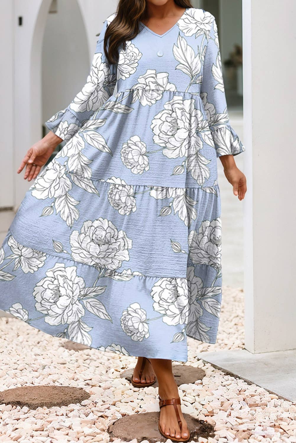 Woman wearing a blue floral dress standing on pebbles with a white archway in the background