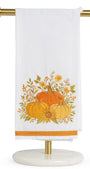 A white kitchen towel with an embroidered autumn harvest design featuring pumpkins, sunflowers, and leaves, hanging from a gold metal stand on a white background.