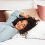Woman lying on a bed with a smile, wearing a light blue sweater.