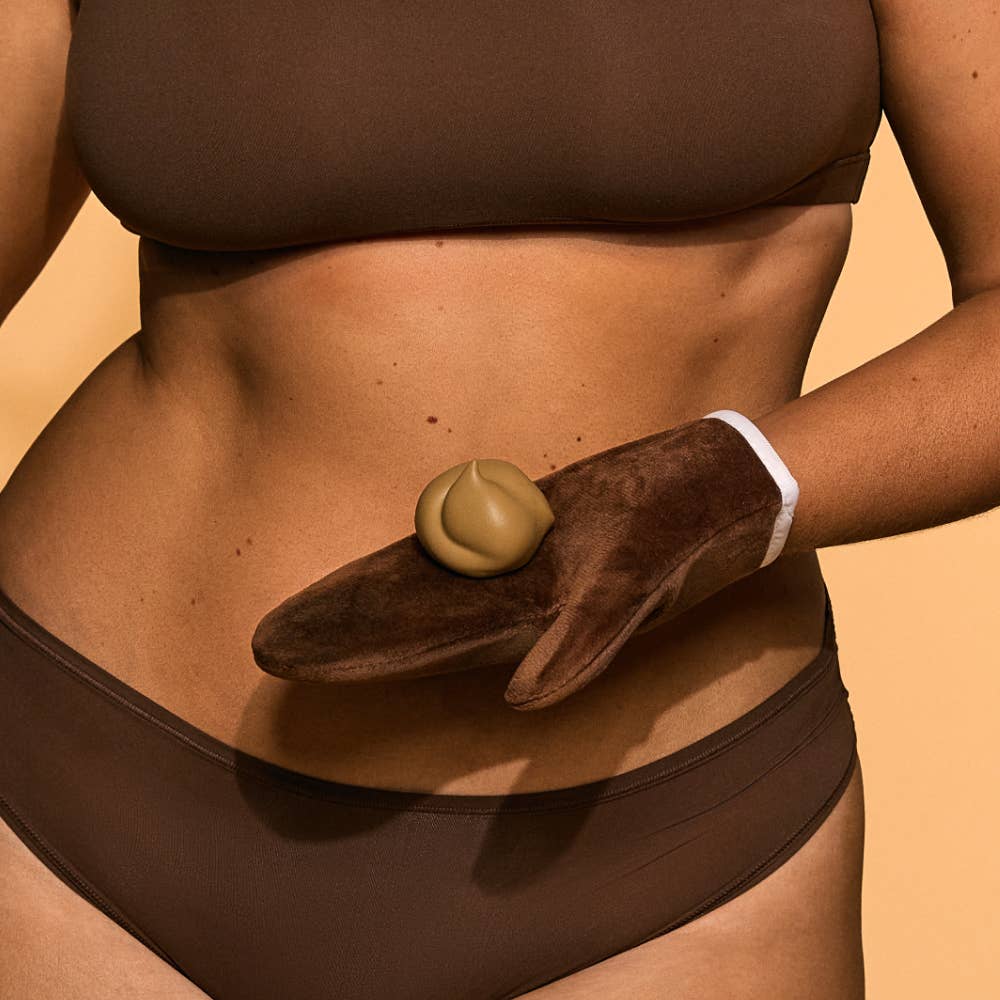 Person wearing a brown bikini with a hand holding self tanning mousse against a beige background