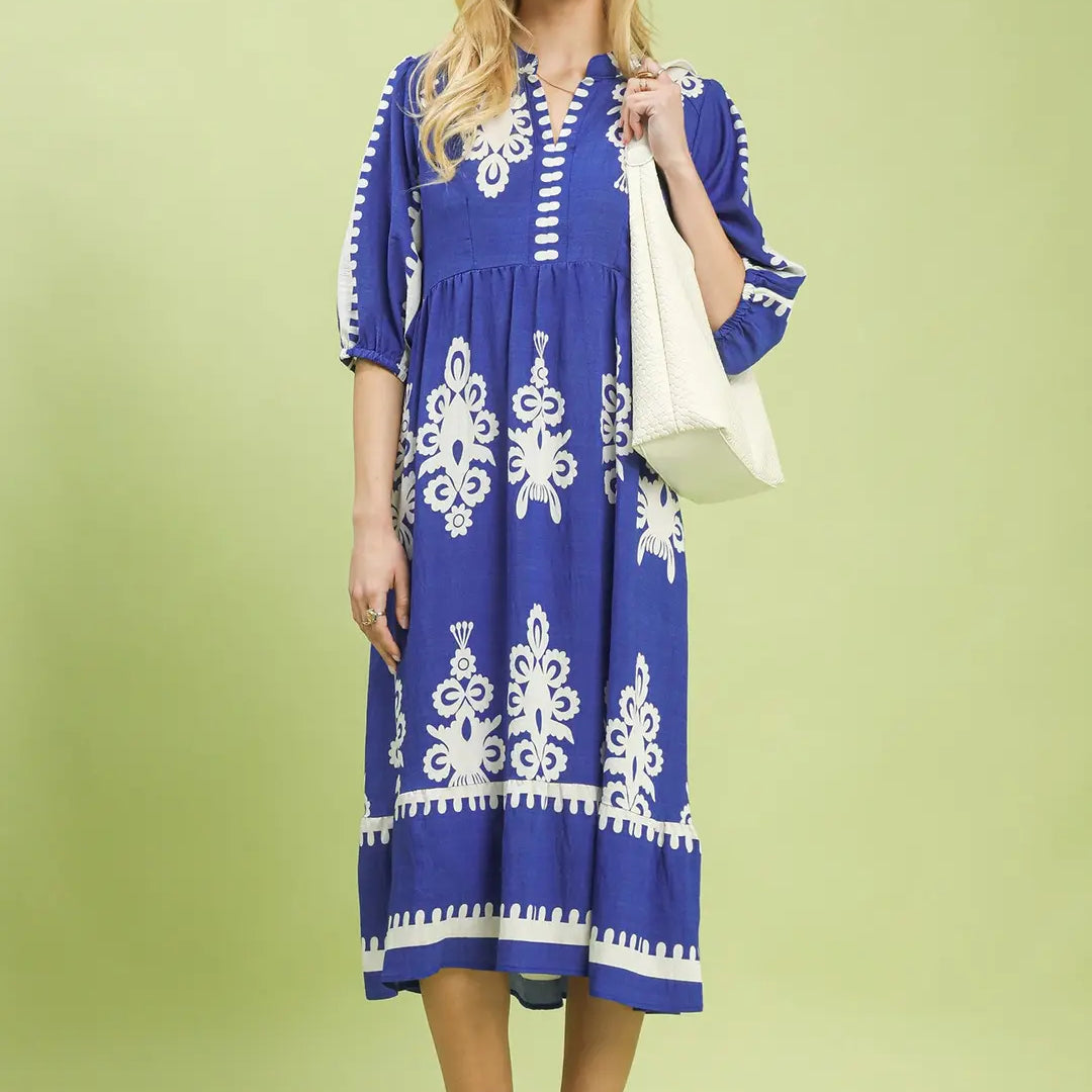 Woman wearing a cobalt blue dress with white patterns on a light green background